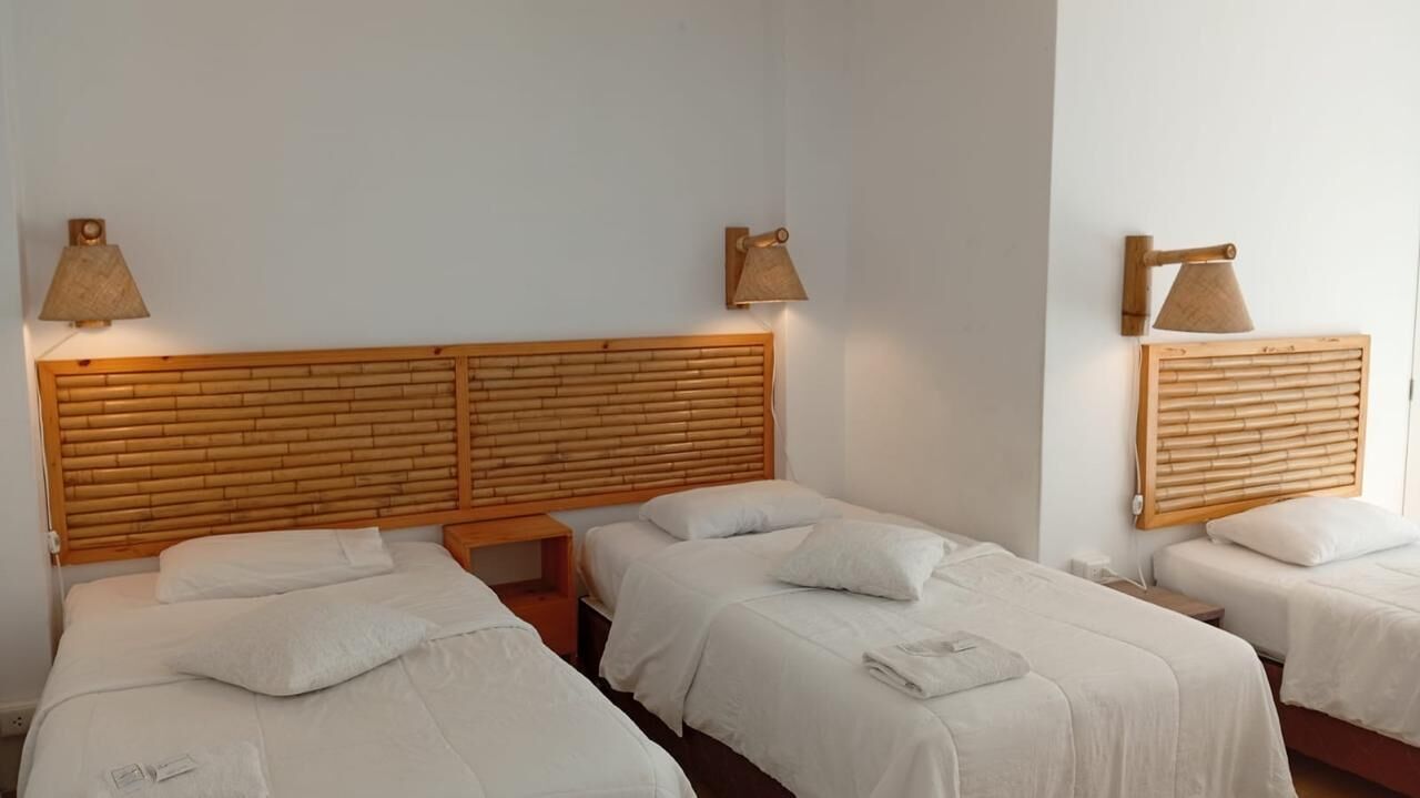 Habitación de hotel con dos camas individuales, cada una con ropa blanca y cabeceros de madera. Hay dos lámparas fijadas a la pared a cada lado de los cabeceros.