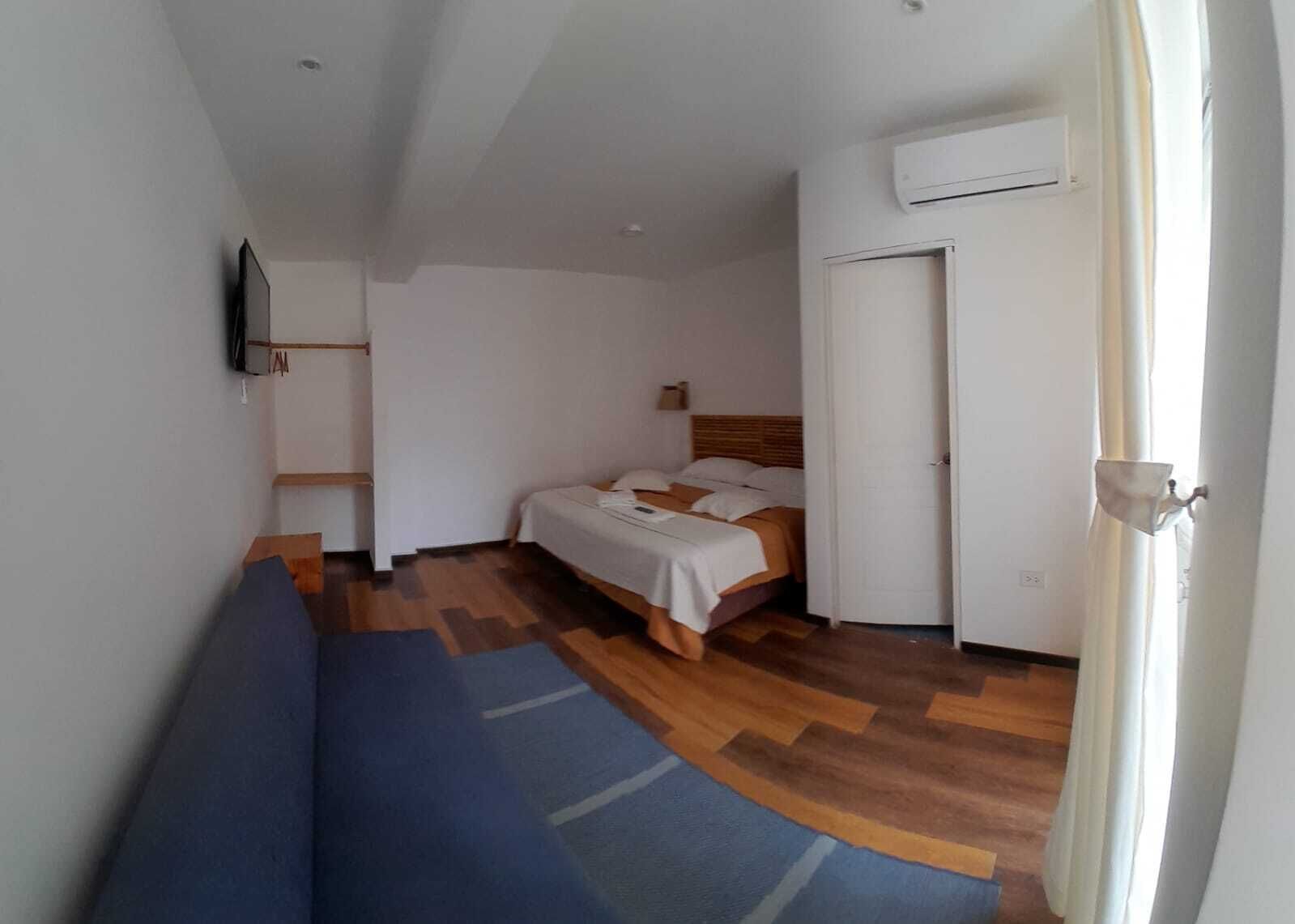 A narrow room with a bed, a blue sofa, a wooden floor, and a white door.
