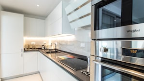 Una cocina moderna con muebles blancos, encimera negra y electrodomésticos de acero inoxidable, incluyendo un horno Whirlpool y una estufa empotrada.