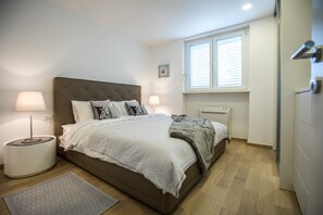 Une chambre à coucher avec un grand lit, deux lampes de chevet, un radiateur et une fenêtre avec des stores.