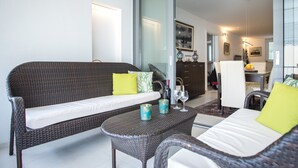 Una sala de estar moderna con mobiliario de mimbre, un ventanal de vidrio que da a un comedor y una cocina al fondo.