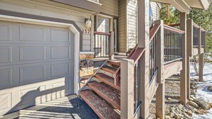 A house with a garage door, a stone accent wall, and a wooden staircase leading to a porch.