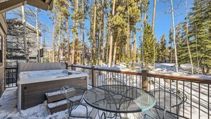 A covered outdoor area with a hot tub, metal chairs, and a snow-covered deck.