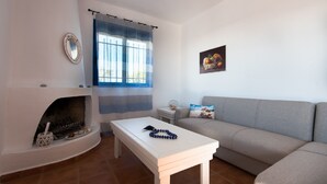 A living room with a fireplace, a sofa, a table, and a window with curtains. - Nautilus Beach House (Rhodes)