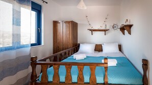 A bedroom with a wooden bed frame, a window with blue curtains, a wardrobe, and a wall-mounted shelf with decorative items. - Nautilus Beach House (Rhodes)