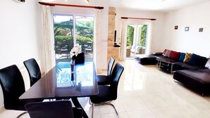A modern living room with a dining area, a black sofa, and a glass-top table with chairs. - Villa Talassa near Coral Bay with optional 4x4 CAR, Jacuzzi and HEATED POOL (Paphos)