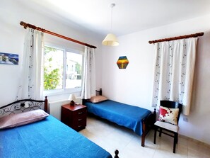 Una habitación con dos camas individuales, una mesita de noche de madera, una silla, una pequeña mesa y una lámpara fijada a la pared.