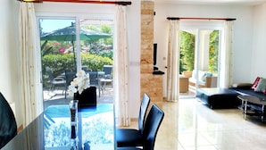 A modern dining area with a glass table, chairs, and a vase of flowers. There is a view of an outdoor patio with a table and chairs, and a sofa in the living area. - Villa Talassa near Coral Bay with optional 4x4 CAR, Jacuzzi and HEATED POOL (Paphos)