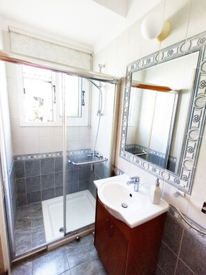 Un baño con cabina de ducha de vidrio, un lavabo blanco y un espejo grande con marco decorativo.