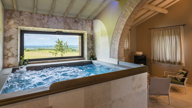 A spa area with a hot tub, a view of the outdoors, and a seating area with a chair and a table. - Villa I Cipressini Tuscany Private luxury pool spa (Pienza)