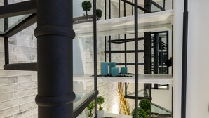 Un interior moderno con una escalera de cristal, barandales de metal y una pared de ladrillo.