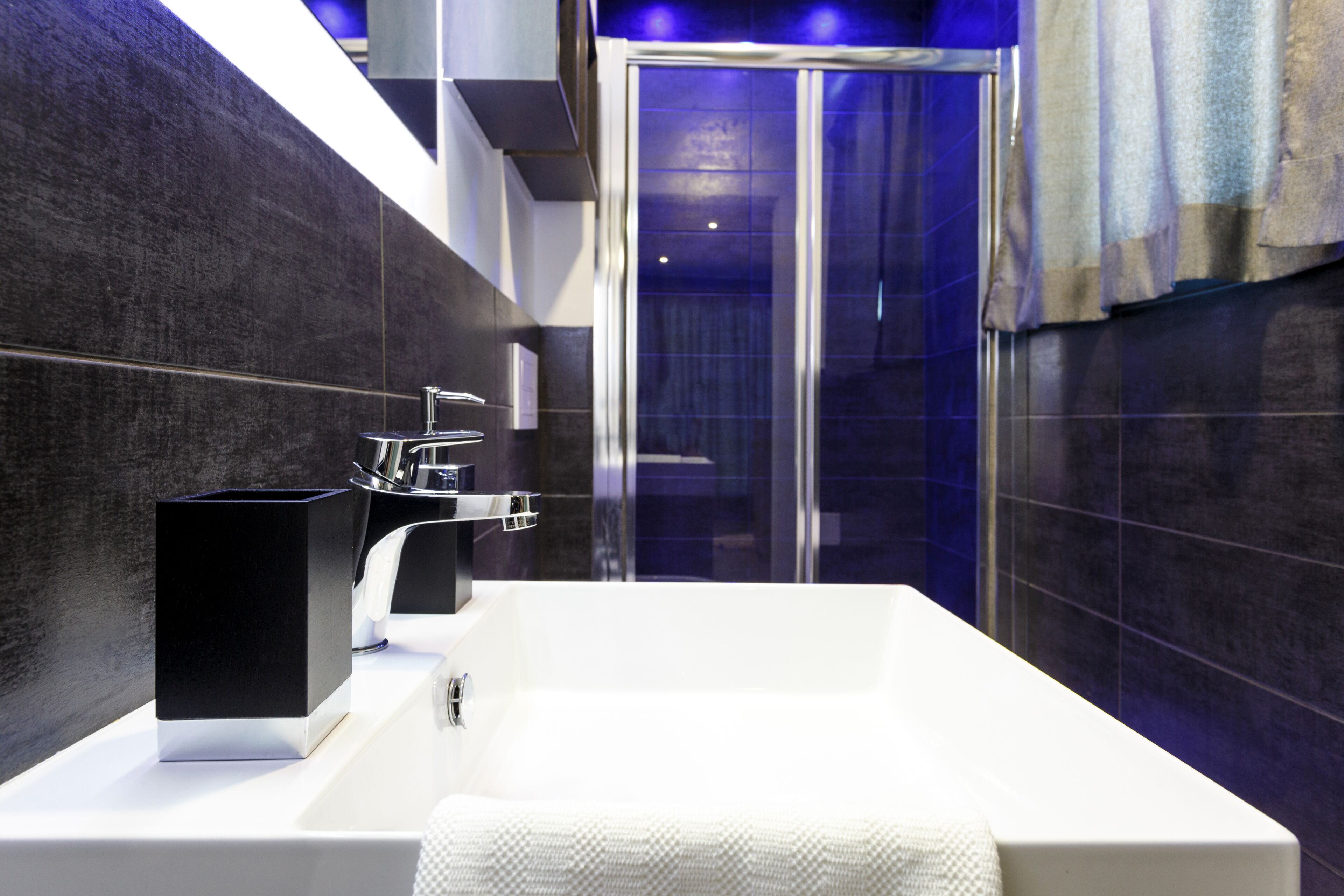 A modern bathroom with a white bathtub, a black soap dispenser, and a glass shower enclosure.
