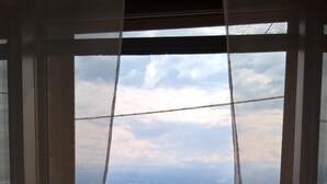 Ein Zimmer mit Blick auf ein grünes Tal und ferne Berge durch ein Fenster mit transparenten Vorhängen.