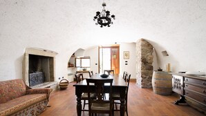 Ein rustikaler Raum mit Kamin, Holzespeisesaal und Stühlen. Es gibt eine Steinwand und ein Holzfass.