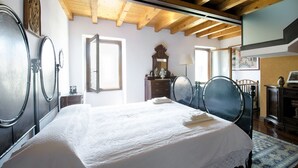 Ein Schlafzimmer mit Holzboden, einem großen Bett mit weißer Bettdecke, zwei runden Spiegeln, einer Kommode und einem Fenster.