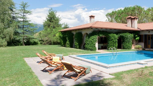 Una casa con piscina, mobiliario de jardín y un jardín.