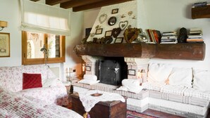 Una habitación acogedora con chimenea, un sofá, una mesa con una manta y una estantería con libros y objetos decorativos.