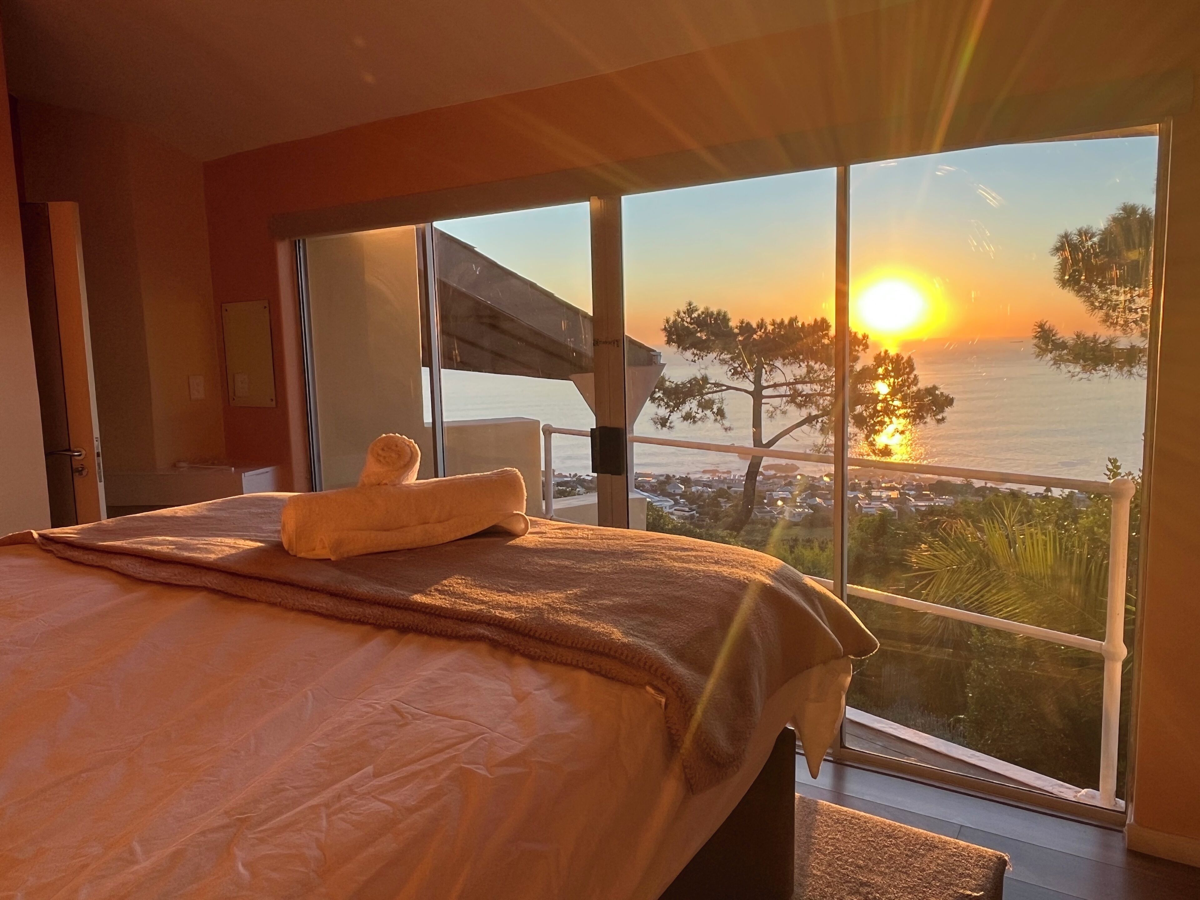 Una camera da letto con un'ampia finestra vista mare al tramonto.
