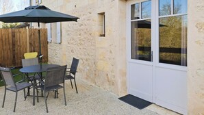 Une terrasse avec une table et des chaises, une clôture en bois et un bâtiment aux murs de pierre et à la porte blanche.