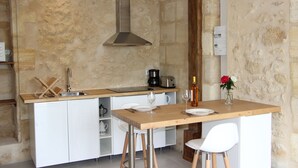 Une cuisine dotée d’un îlot central, de meubles blancs, d’une hotte en acier inoxydable et d’un mur en pierre en arrière-plan.
