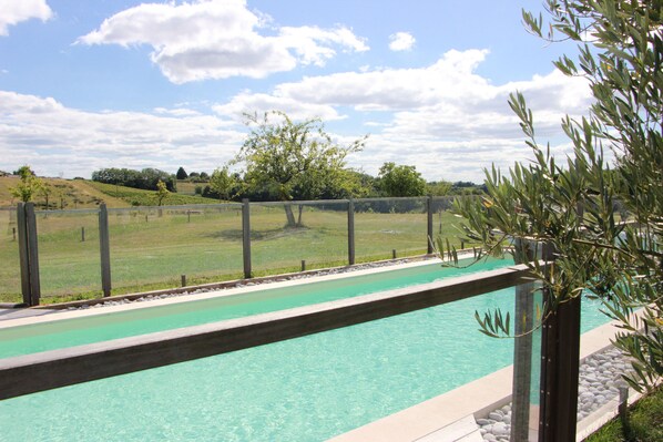 A swimming pool with a wooden deck and a view of a grassy landscape.