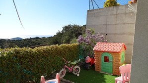 Un espace de jeux pour enfants avec un toboggan, une petite maison et un tricycle rose.