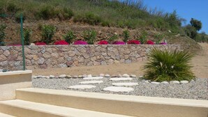 Une série de marches de couleur beige menant à un mur de pierre, avec un jardin de fleurs roses et une petite plante verte.