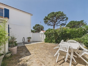 Un espace patio avec une table et des chaises blanches, une plante en pot et une clôture blanche.