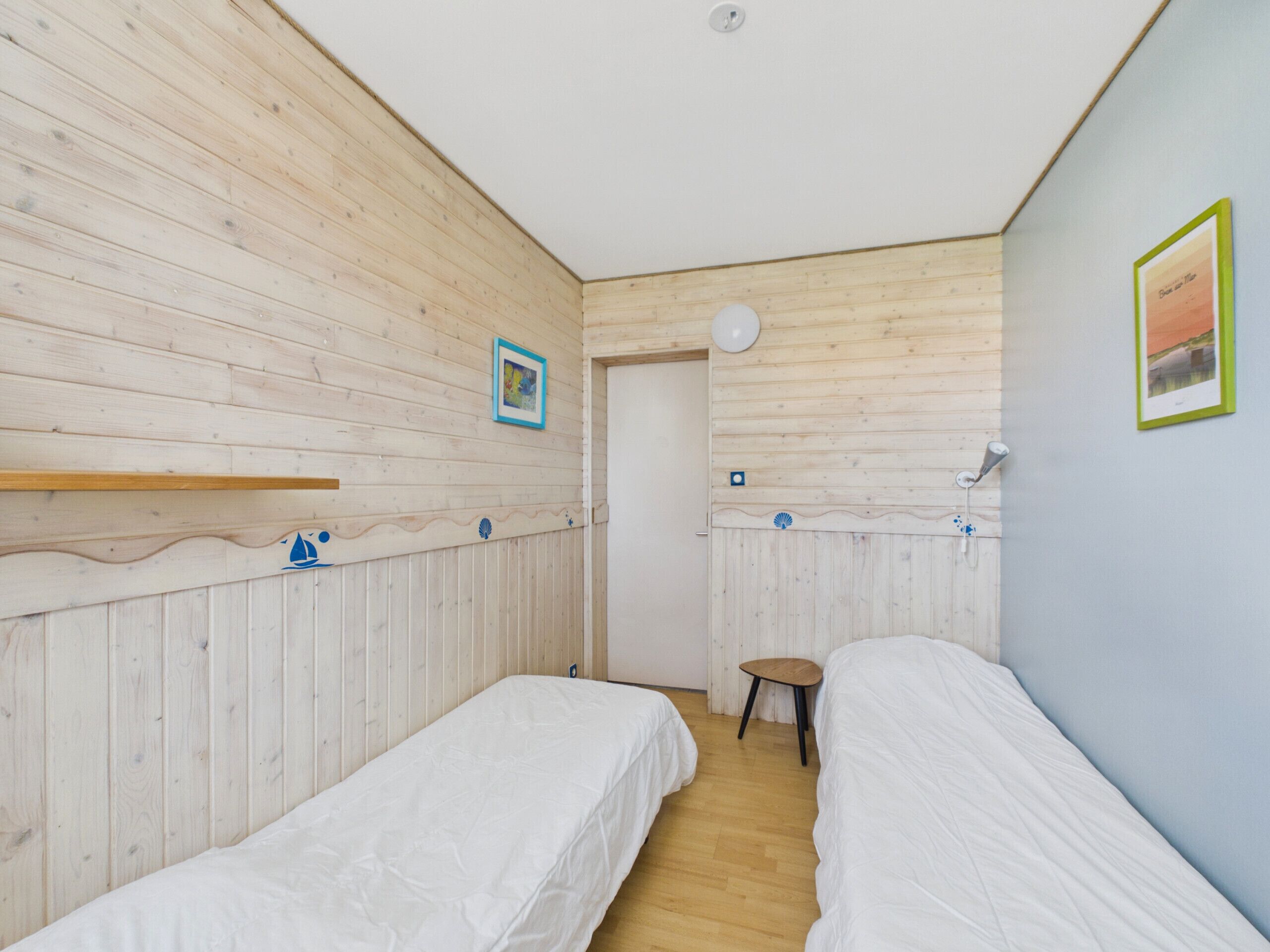 A room with two single beds, wooden walls, a small stool, and a door leading to another room.