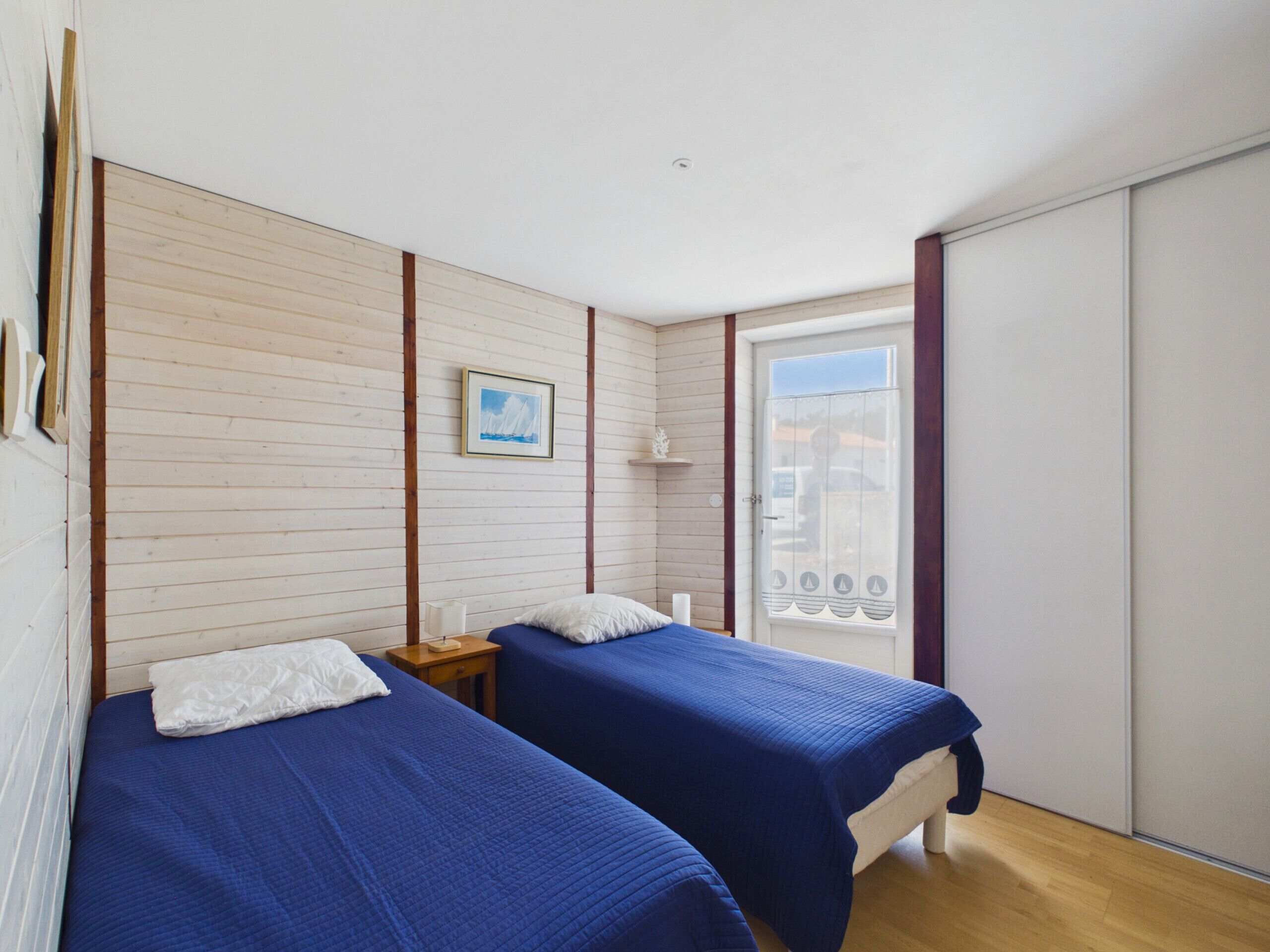 A room with two beds, a wooden wall, a framed picture, and a window with a view.