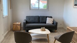 A modern living room with a grey sofa, two grey chairs, a white coffee table, and a window with a view of buildings.