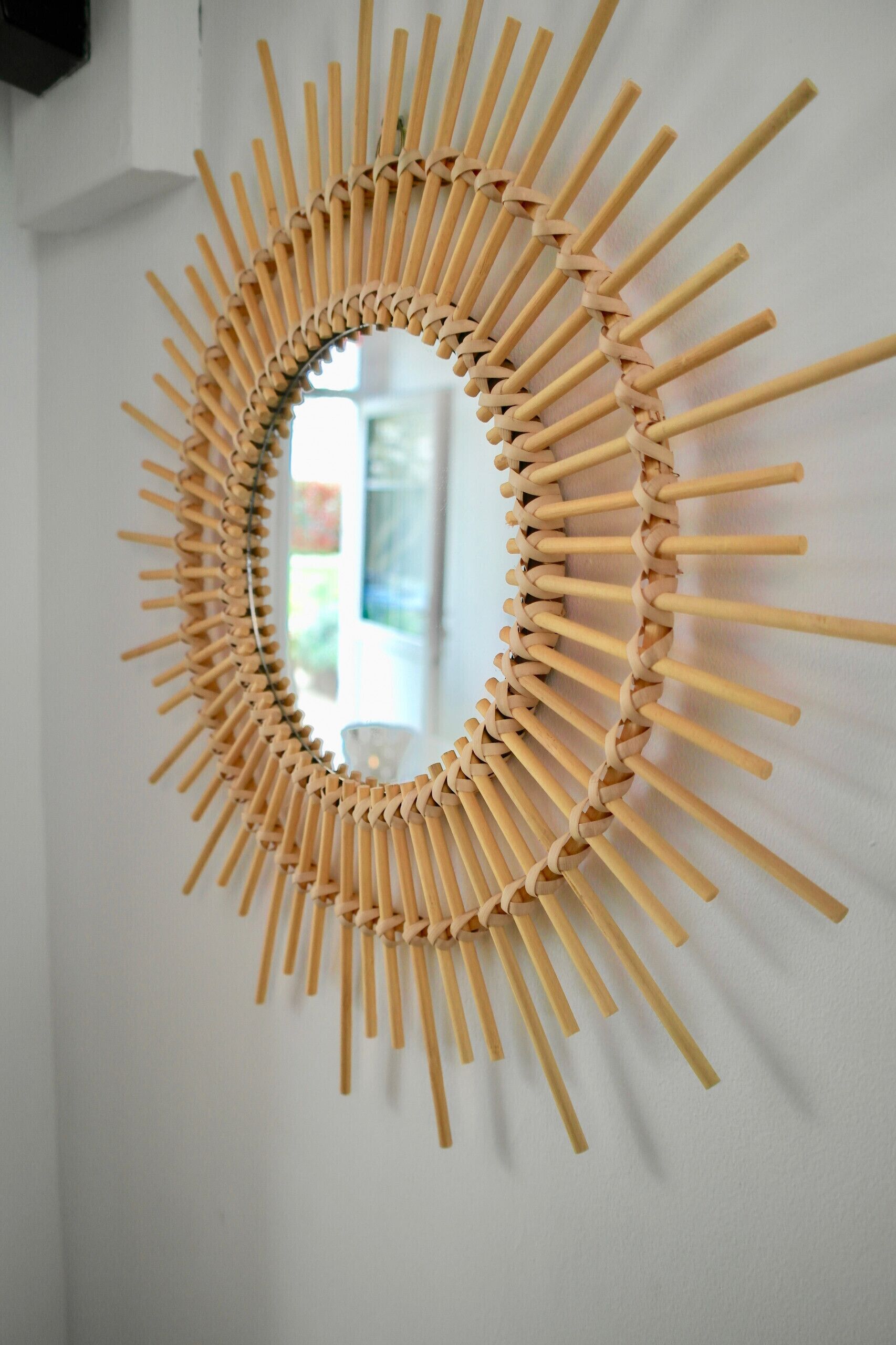 Un espejo montado en la pared con un diseño de sol hecho de palitos de madera.