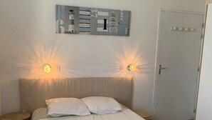 A bedroom with a bed, two bedside lamps, a door, and a wall-mounted artwork.