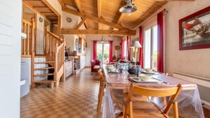 Una cuina àmplia amb bigues de fusta, una taula de dinar preparada per a quatre persones i una escala que condueix a un altre nivell.