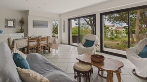 A spacious living area with a sofa, chairs, a dining table, and a view through large sliding glass doors. - 150m from the beach - Maison vendéenne for 6 (Bretignolles-sur-Mer)