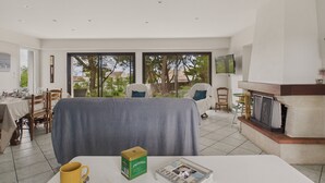A spacious living room with a dining area, a fireplace, and large windows offering a view of the outdoors. - 150m from the beach - Maison vendéenne for 6 (Bretignolles-sur-Mer)