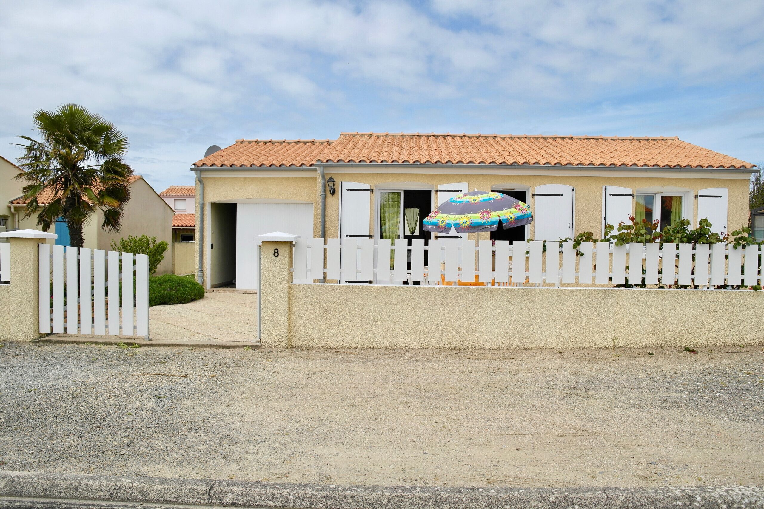 Une maison à deux étages, avec un toit recouvert de tuiles, une clôture blanche en bois et le chiffre « 8 » peint sur la porte.
