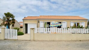 Une maison à deux étages, avec un toit recouvert de tuiles, une clôture blanche en bois et le chiffre « 8 » peint sur la porte.