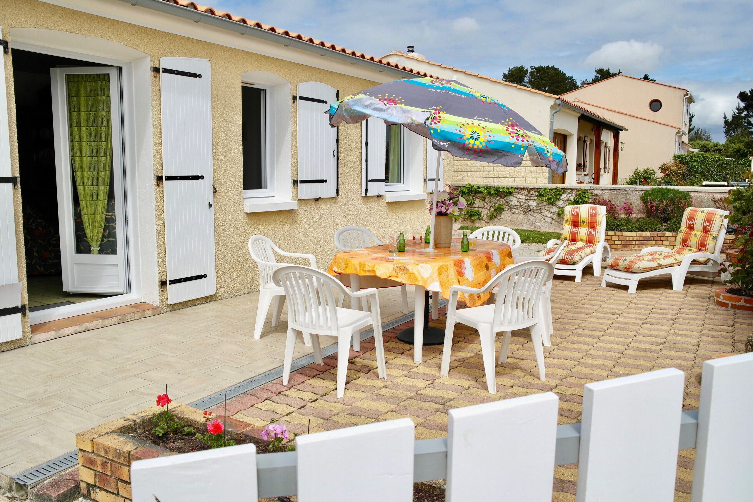 Um pátio com mesa e cadeiras, um guarda-sol colorido e uma parede de tijolos.