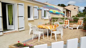Une terrasse avec une table et des chaises, un parasol coloré et un mur en briques.