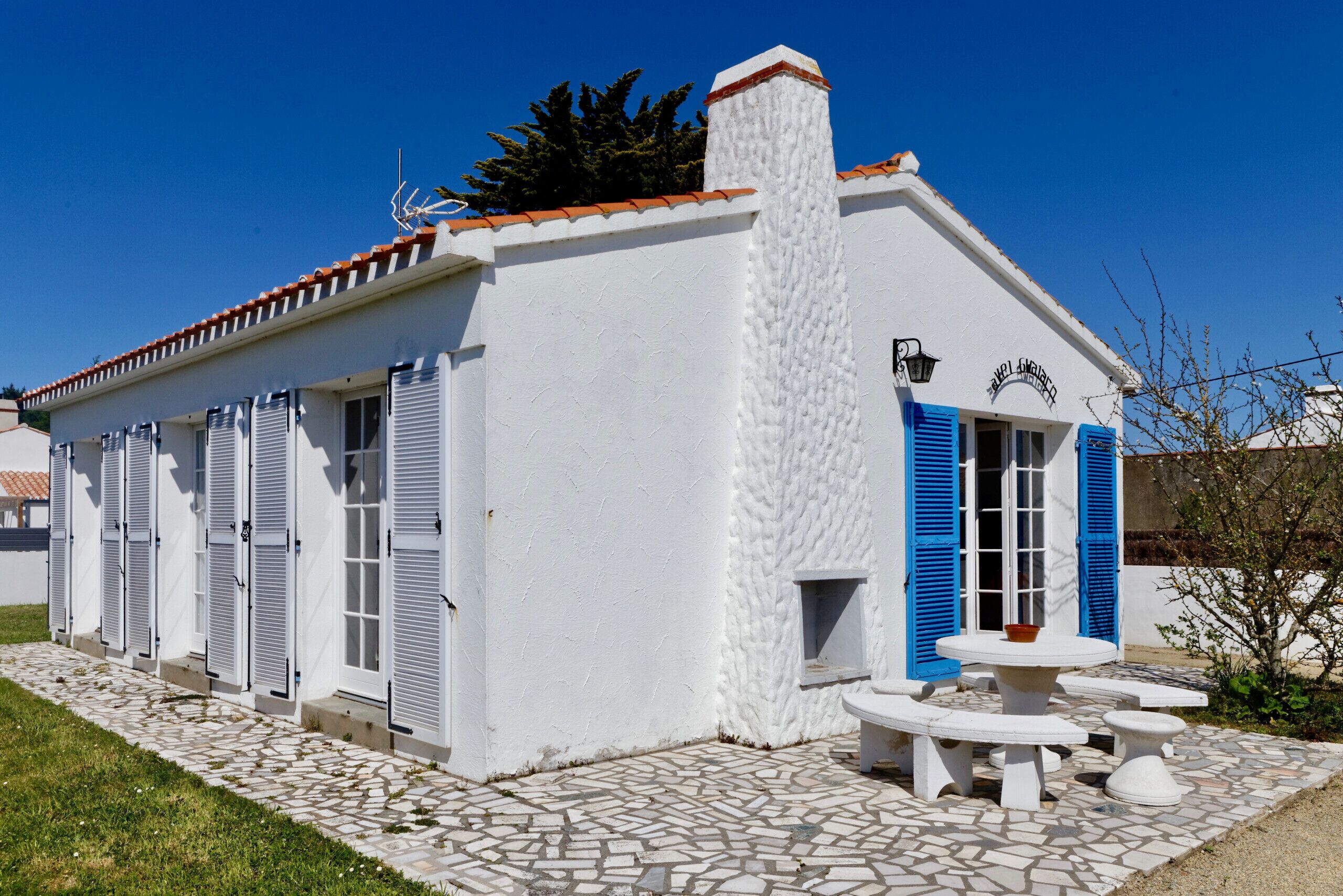 Un edificio blanco con contraventanas azules, un patio empavedado y una chimenea.