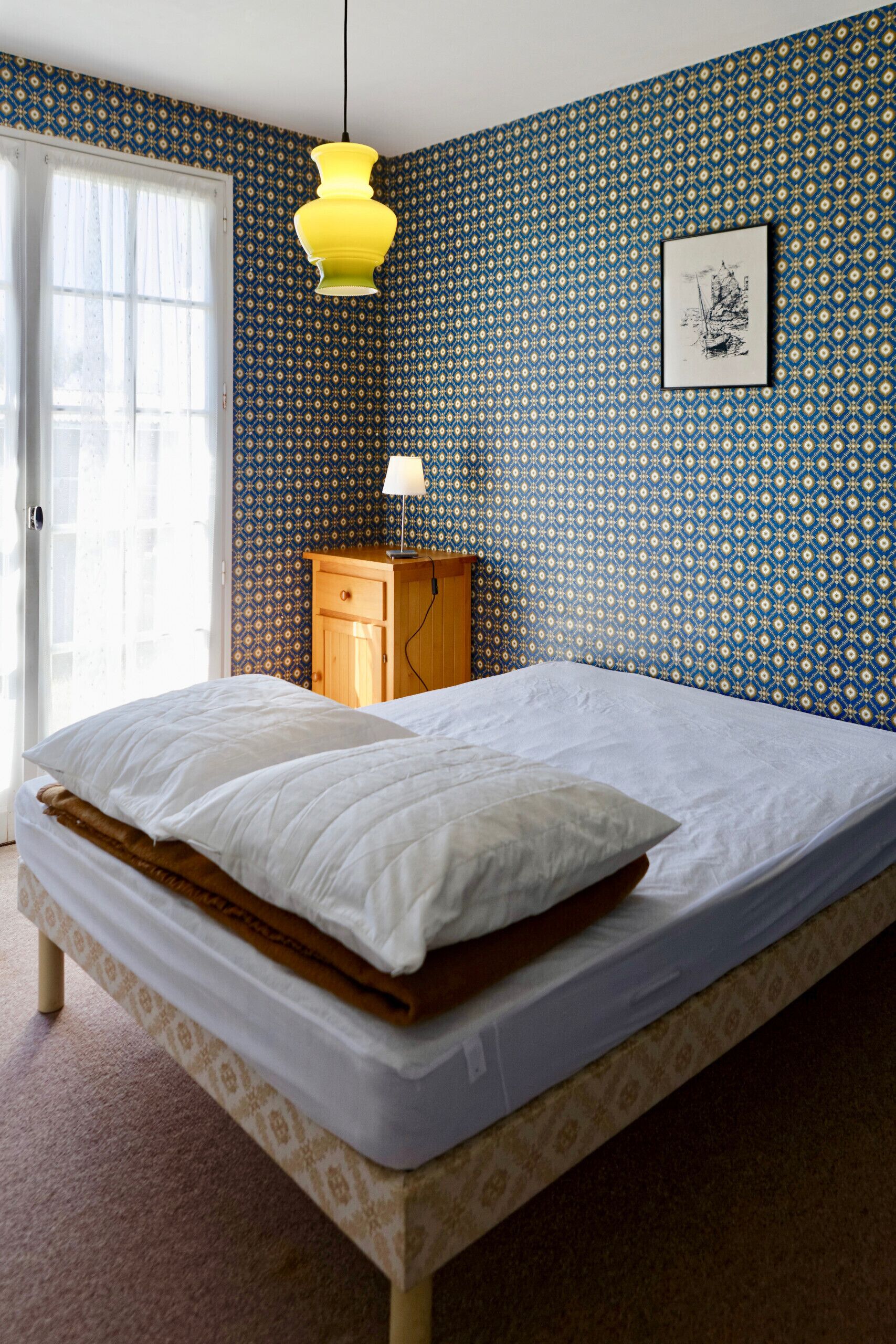 Une chambre à coucher avec un lit, une table de chevet en bois, une lampe et un mur décoré d’un motif.