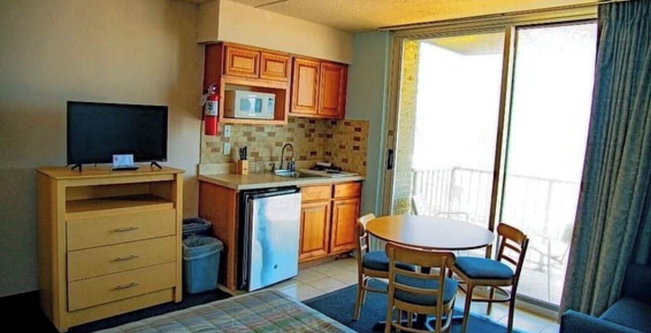 A compact kitchen with a microwave, sink, and wooden cabinets. There's a small dining area with a table and chairs.