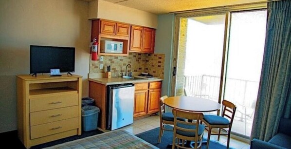 A compact kitchen with a microwave, sink, and wooden cabinets. There's a small dining area with a table and chairs. - Acropolis Oceanfront Resort (North Wildwood)