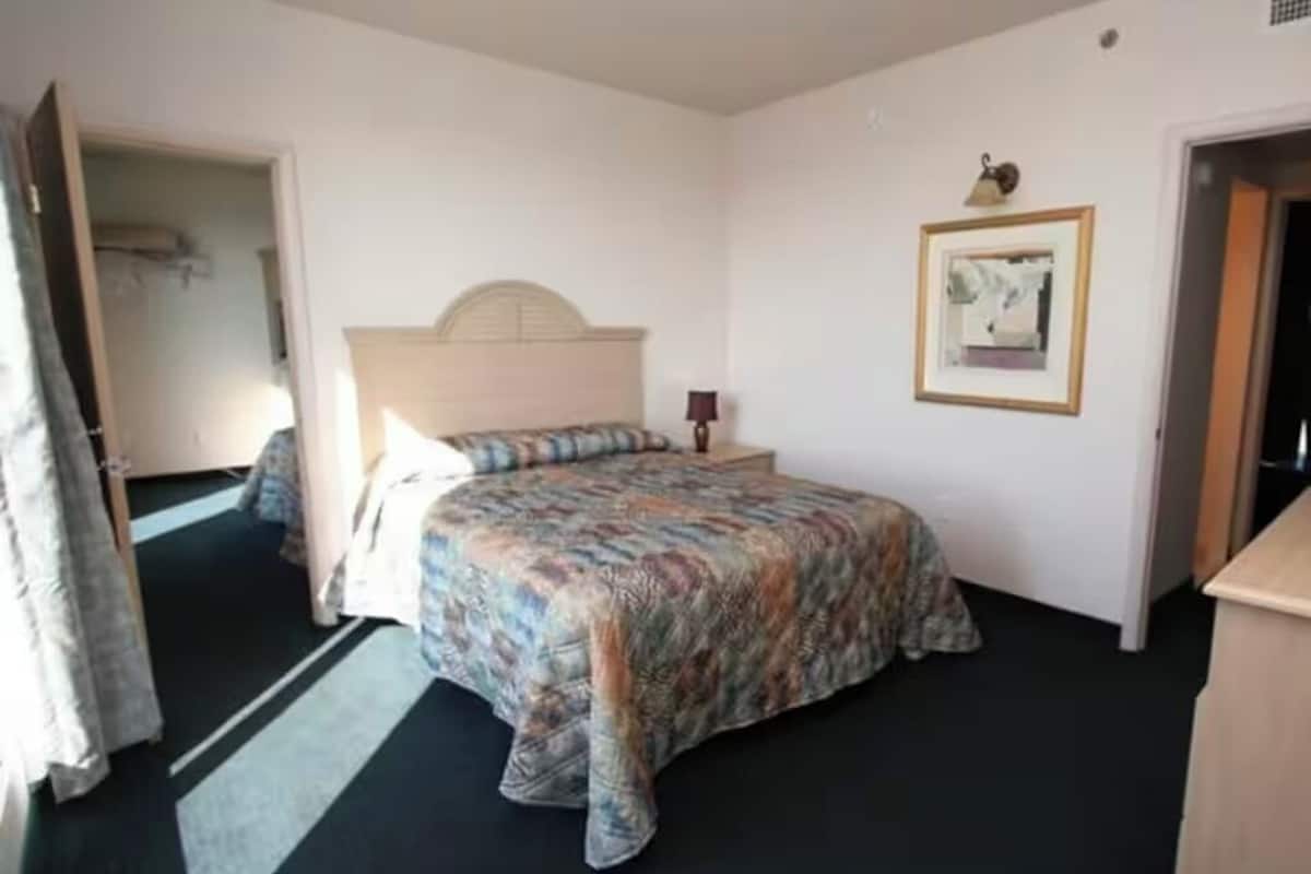 A bedroom with a bed, a nightstand, a framed picture on the wall, and a door leading to another room.