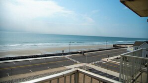 A coastal road with a beach in the background, a pedestrian walkway, and a building with a balcony. - Acropolis Oceanfront Resort (North Wildwood)