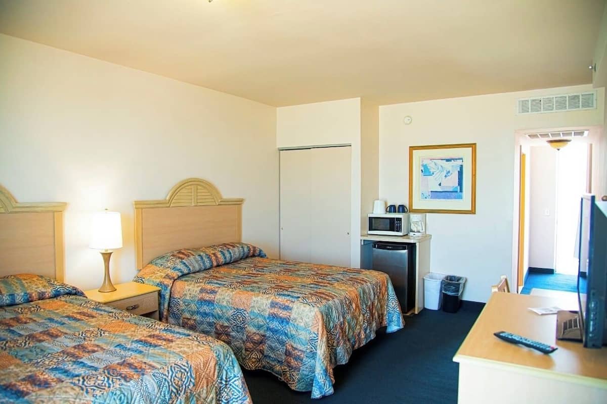 A hotel room with two beds, a desk with a computer, a microwave, and a trash bin.