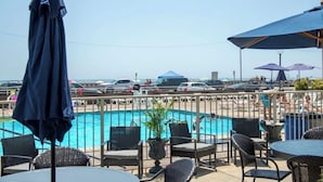 A poolside area with chairs and umbrellas, a view of the sea, and parked cars. - Acropolis Oceanfront Resort (North Wildwood)