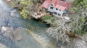 A house by a clear stream with a red roof, surrounded by trees. - Riverside Runaway | Ellijay, GA (Ellijay)