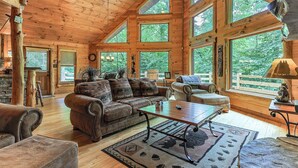 A spacious wooden cabin with a high ceiling, large windows, and a cozy living area with leather furniture. - Serenity on The Mountain | Blue Ridge, GA (Blue Ridge)